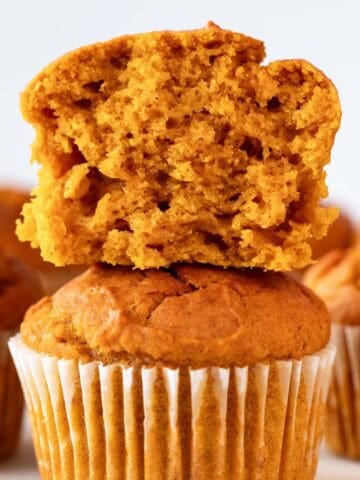 Stacked vegan pumpkin muffins with the top one sliced and more in the background.