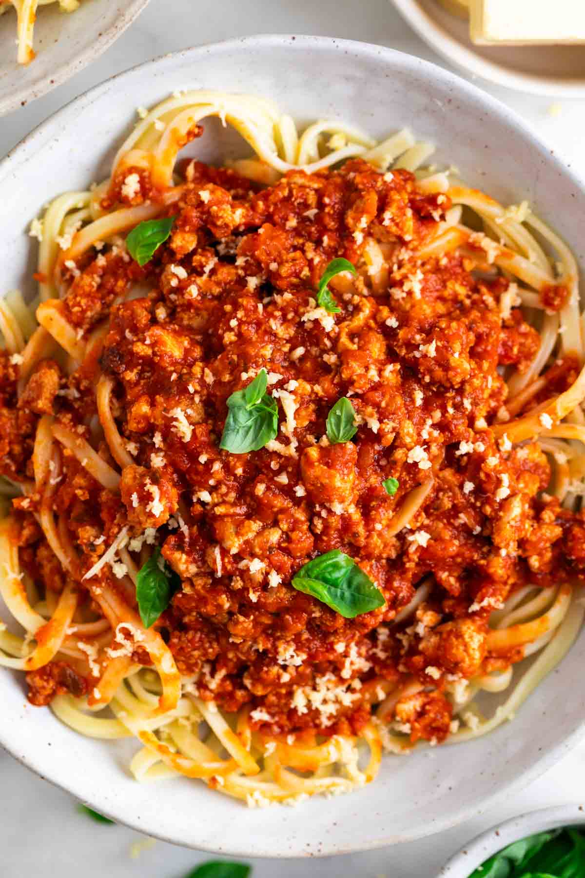 Tofu bolognese over spaghetti garnished with vegan Parmesan and basil.