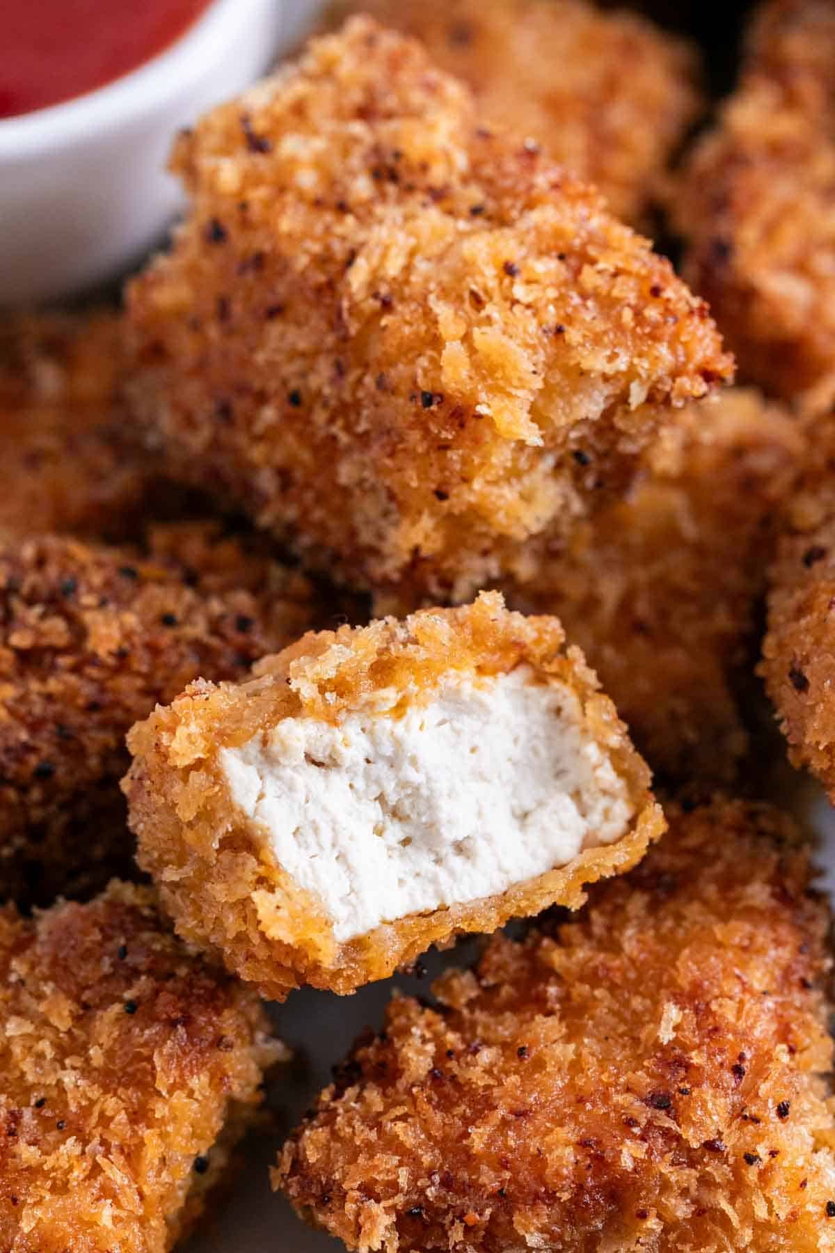 Tofu chicken nuggets with ketchup and a nugget showing the inside.