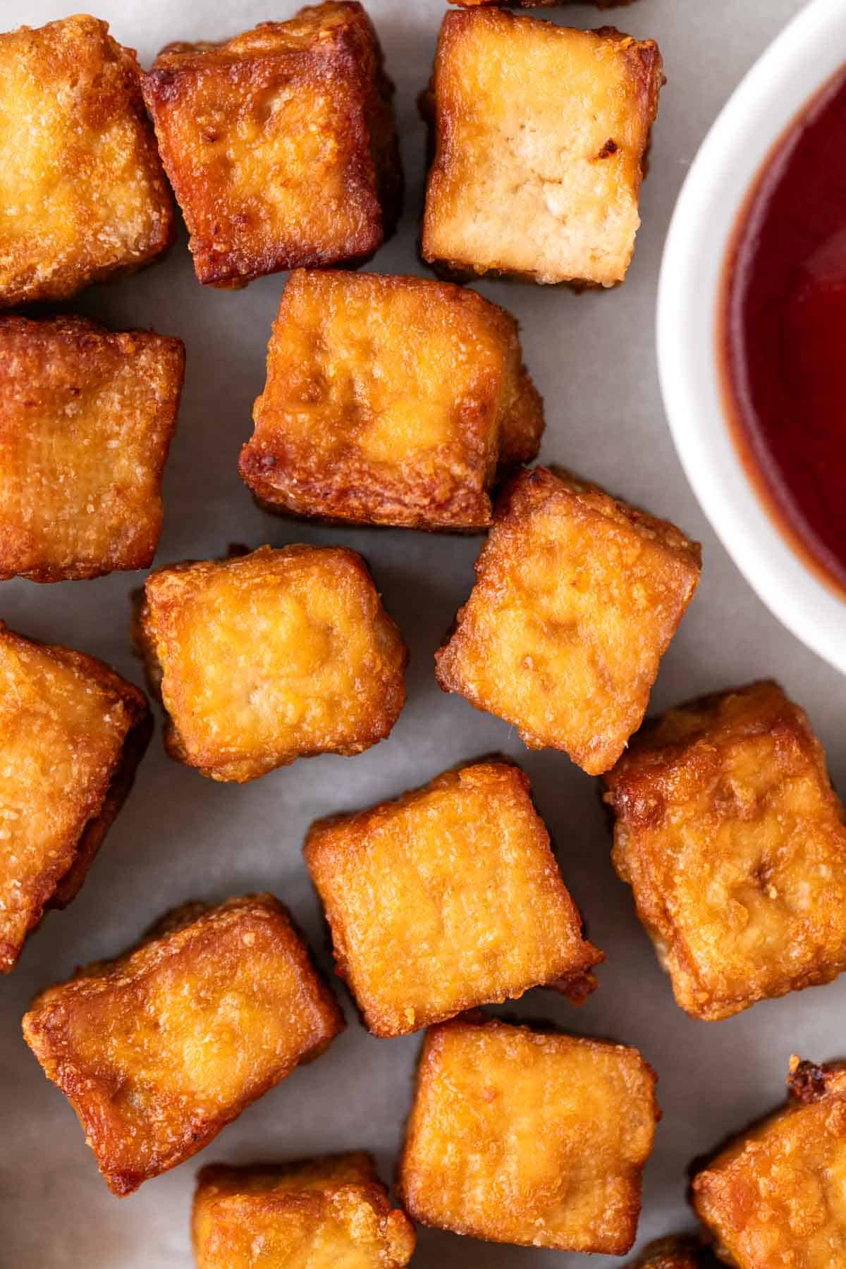 Air fryer tofu on a white background with a small bowl of ketchup.