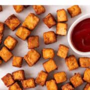 Golden air fryer tofu served on a white backdrop with a small bowl of ketchup.