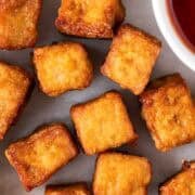 Crispy tofu cubes cooked in the air fryer on a white background with ketchup on the side.