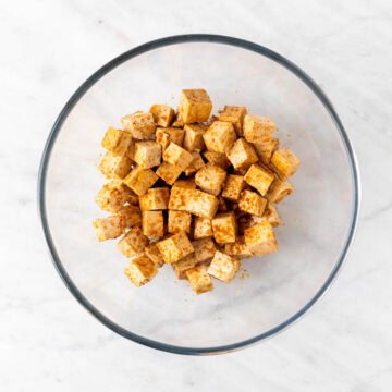 Firm tofu cubes tossed with soy sauce, oil, and garlic powder in a bowl.