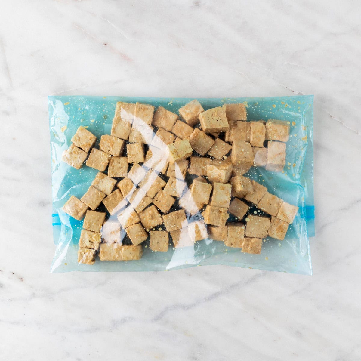 Marinated tofu cubes covered in cornstarch inside a large ziploc bag.
