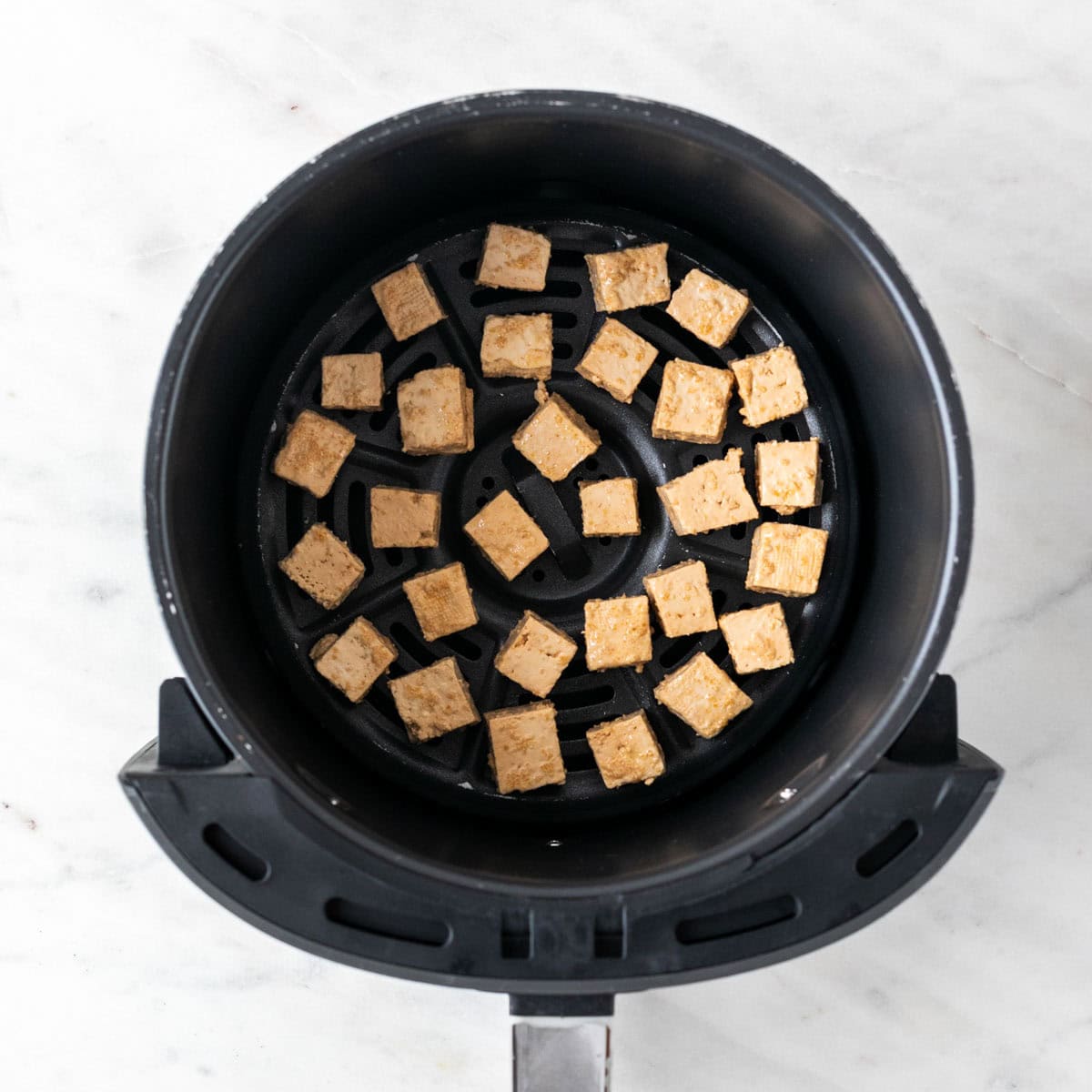 Tofu cubes in the air fryer basket in a single layer before cooking.