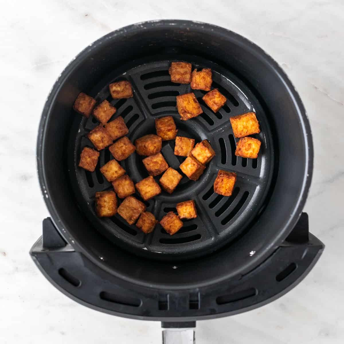 Cooked tofu cubes in the air fryer basket in a single layer.