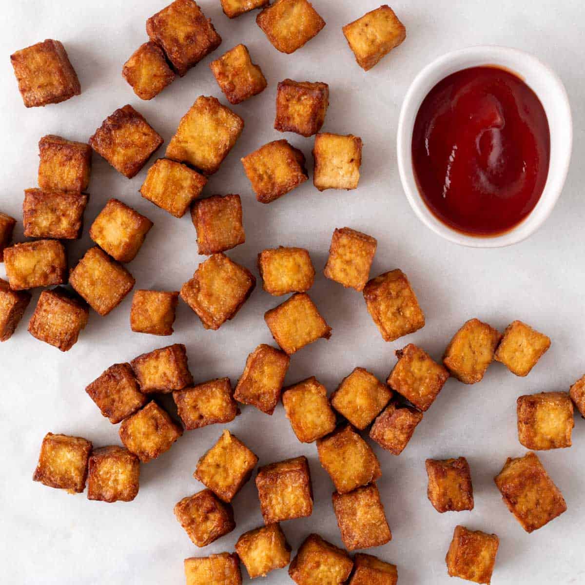 Air fryer tofu arranged on a white plate with a small bowl of ketchup.