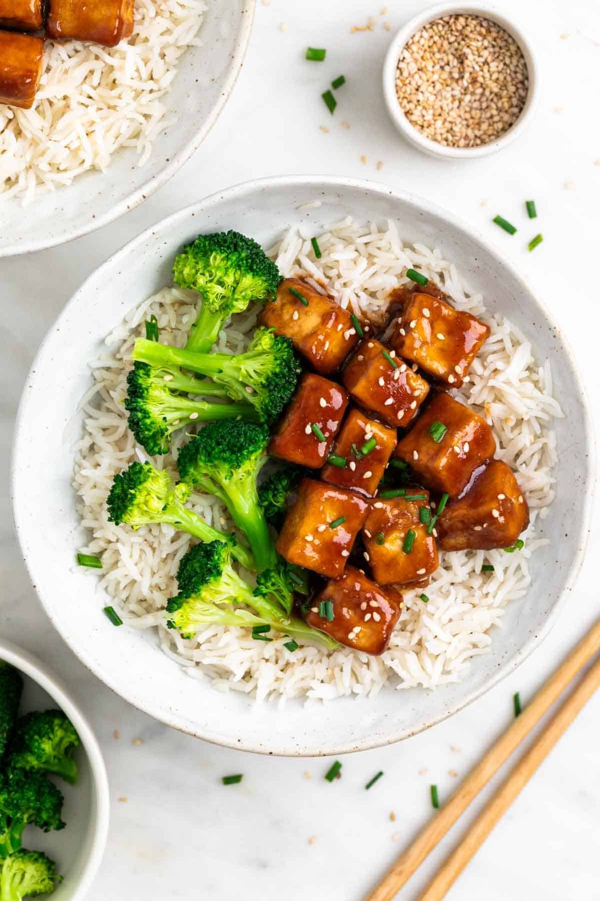 Rice and broccoli bowls topped with teriyaki tofu and served with chopsticks.