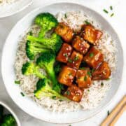 Rice and broccoli bowls topped with teriyaki tofu, sesame seeds, and fresh chives.