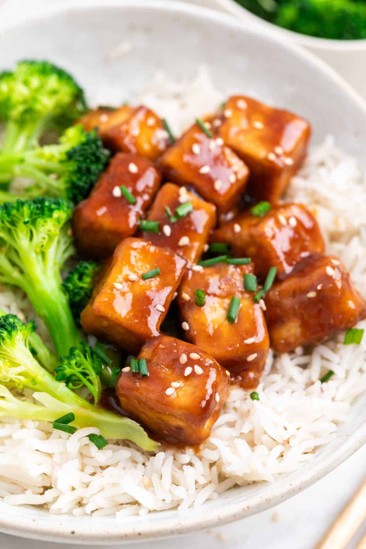 Bowl of teriyaki tofu served with rice, broccoli, sesame seeds, and chives.