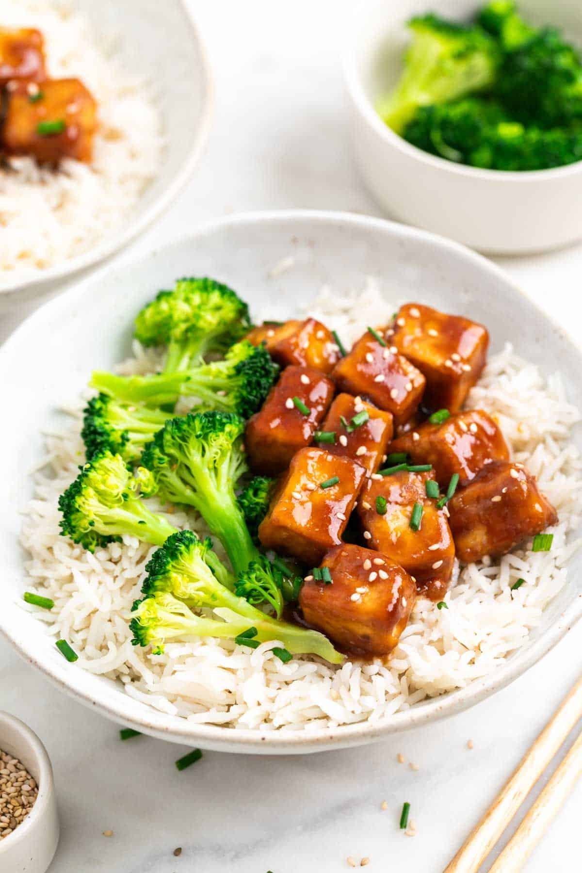 Bowls with rice, broccoli, and teriyaki tofu served with chopsticks.