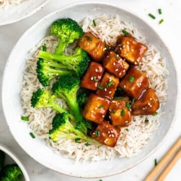 Rice and broccoli bowls topped with teriyaki tofu, sesame seeds, and fresh chives.