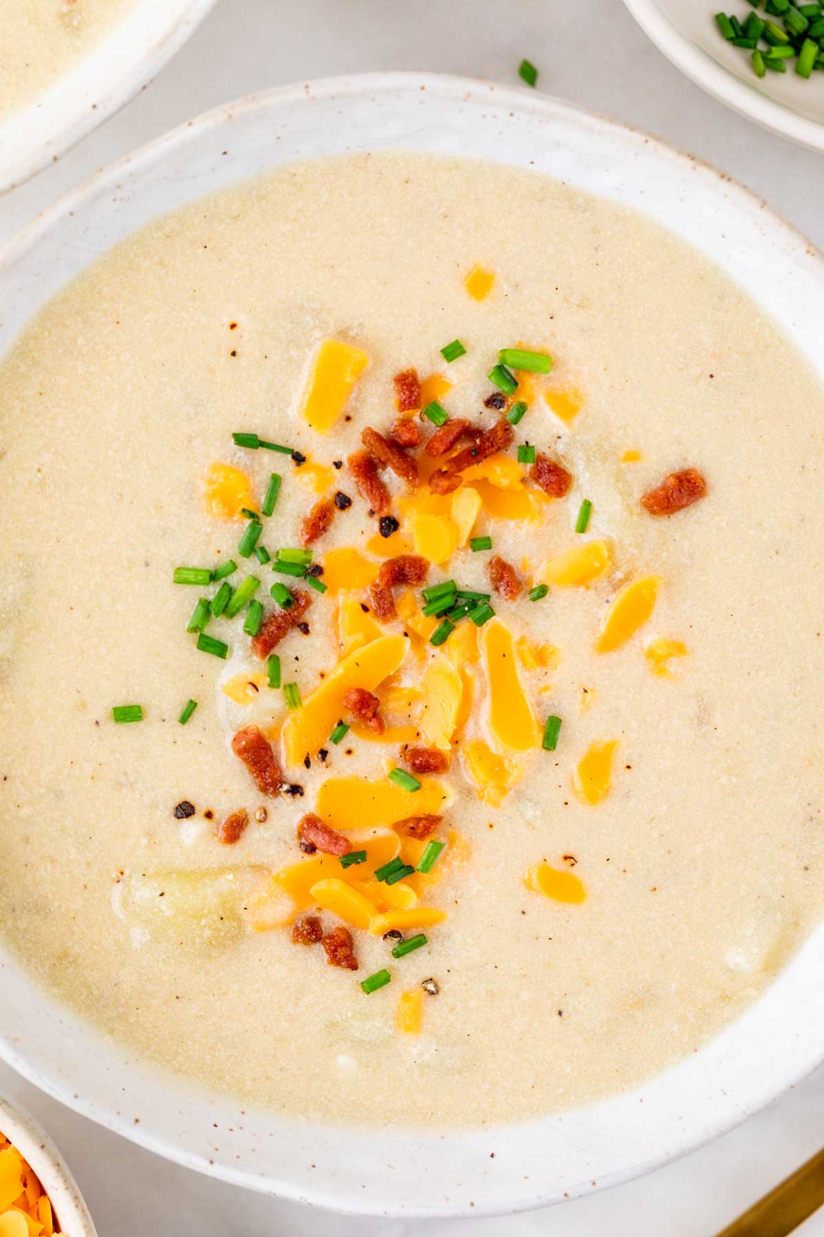 Bowl of vegan potato soup topped with vegan bacon bits, vegan cheddar, and chives.