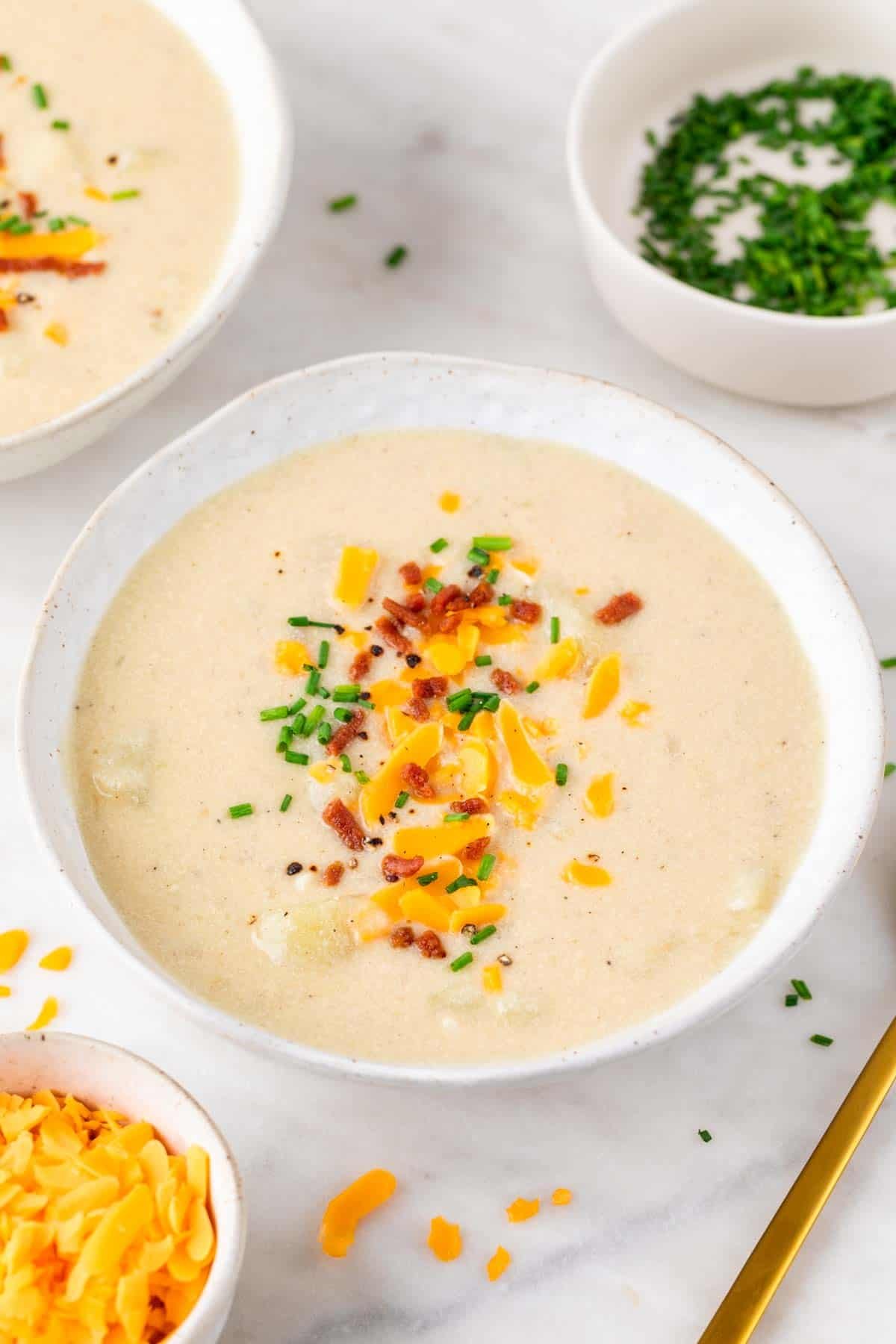 Overhead view of two bowls of vegan potato soup with ingredients on the side.