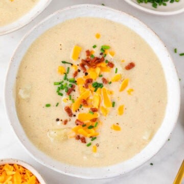 Two bowls of vegan potato soup with ingredients arranged around them.