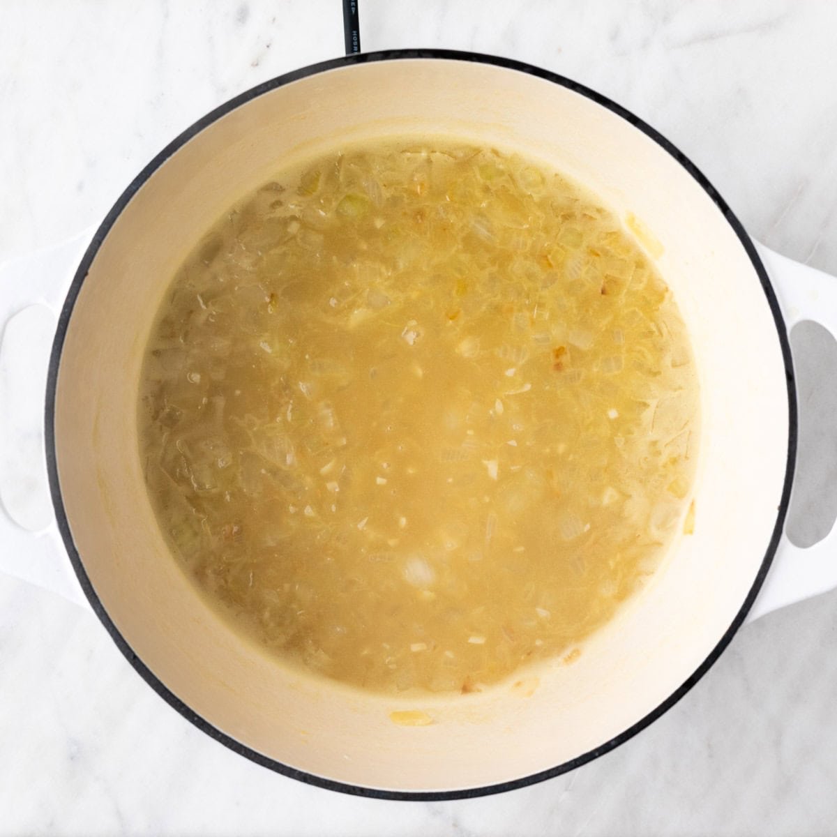 Vegetable broth added to the onion, garlic, and flour mixture in a pot.