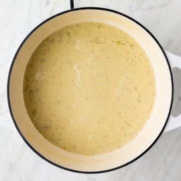 Plant milk, salt, and pepper added to the soup base in a pot.
