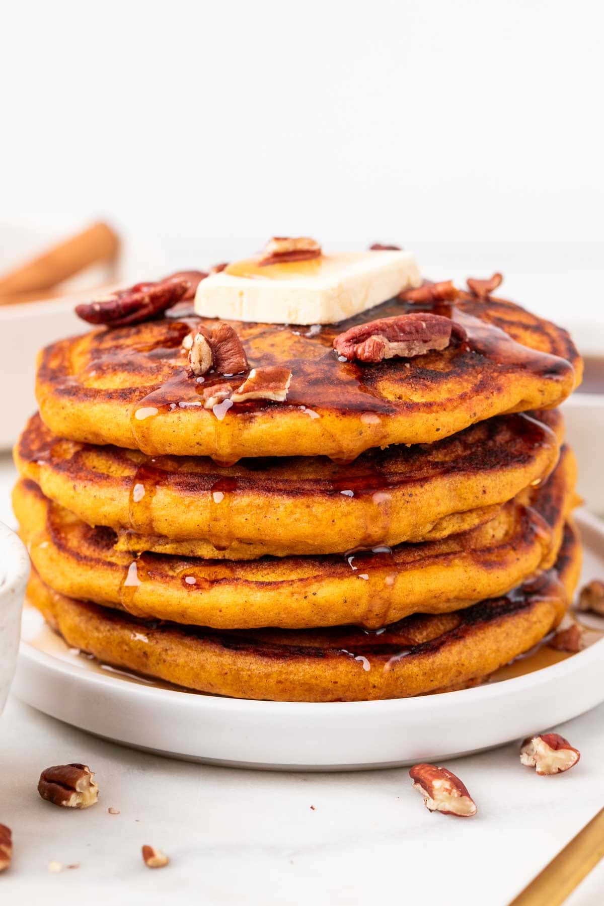 Stack of vegan pumpkin pancakes topped with maple syrup, vegan butter, and pecans.