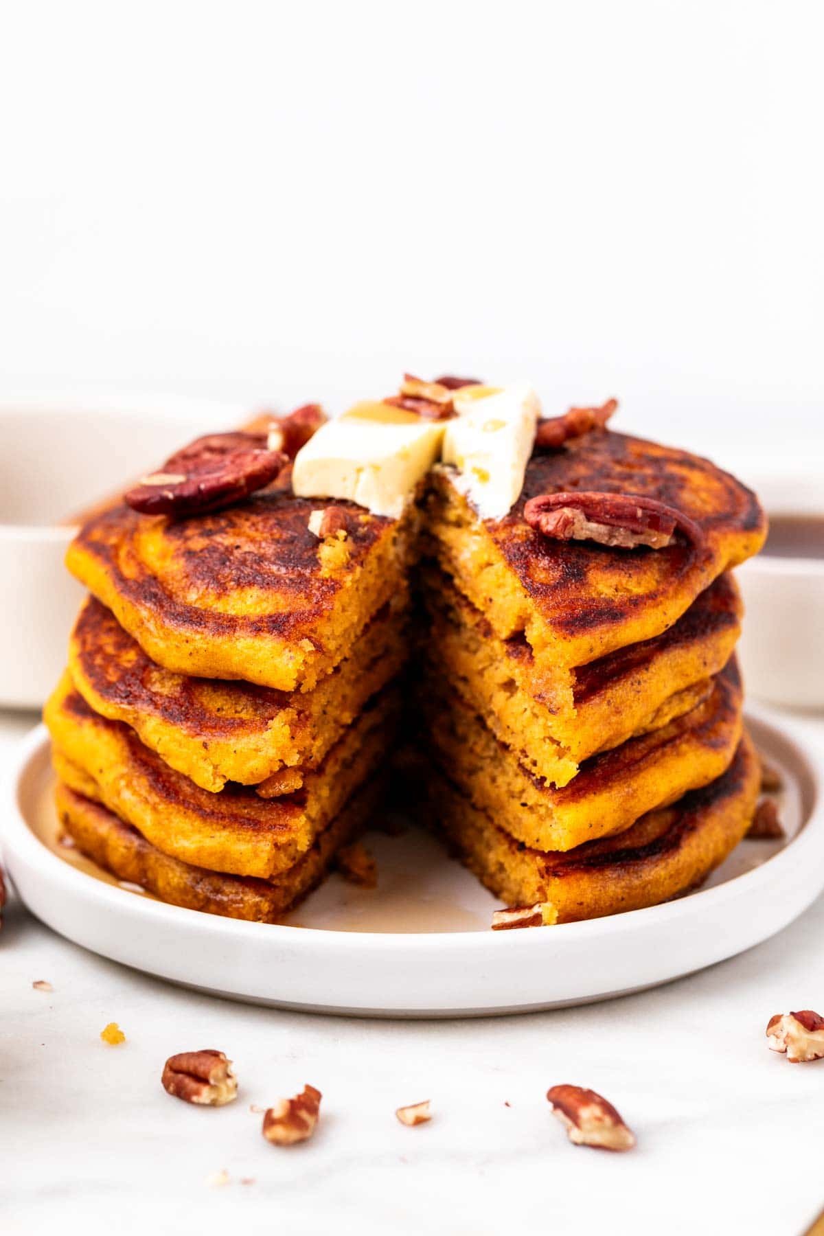 Half-eaten vegan pumpkin pancakes with maple syrup and pecans on top.