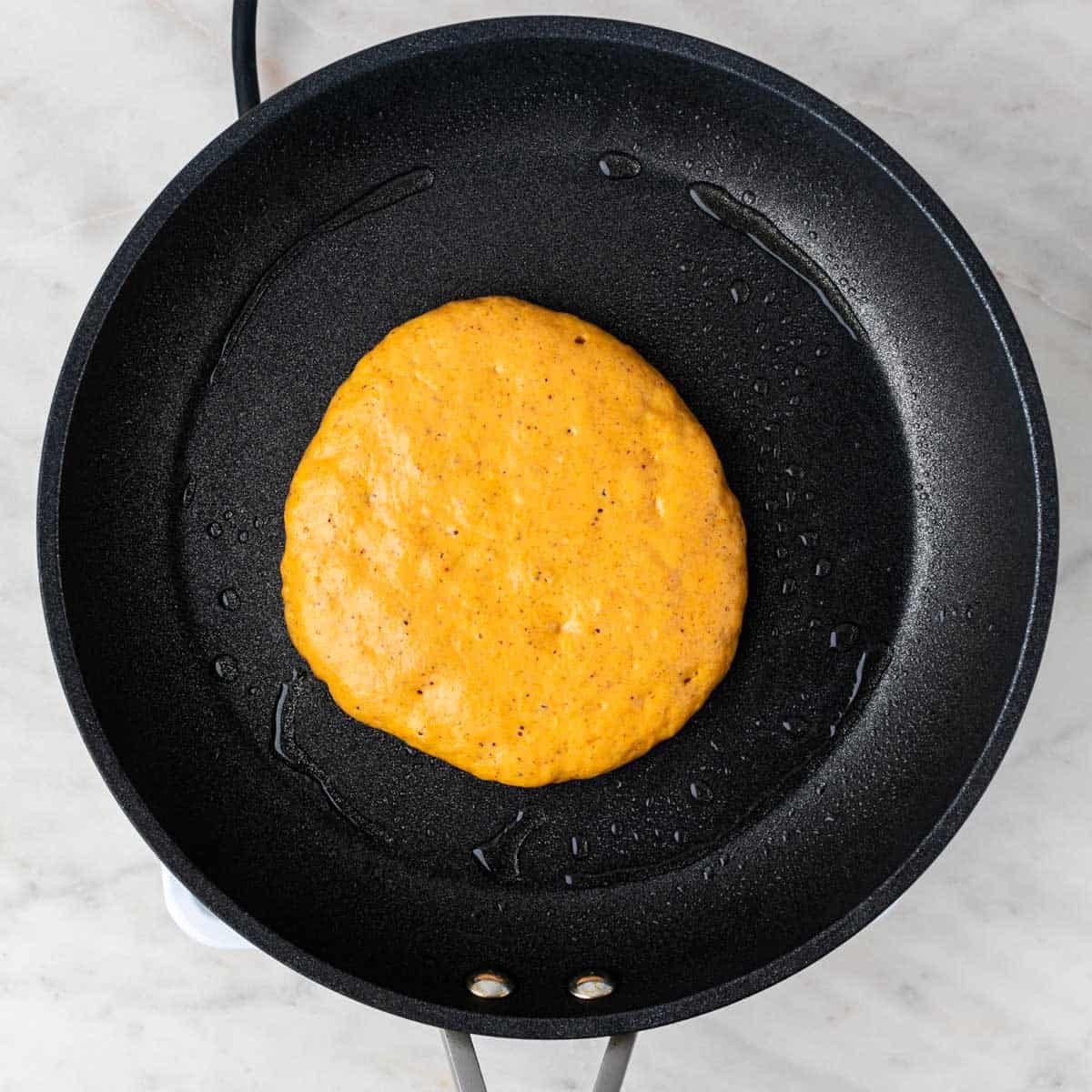 A vegan pumpkin pancake cooking in a greased pan, ready to be flipped.