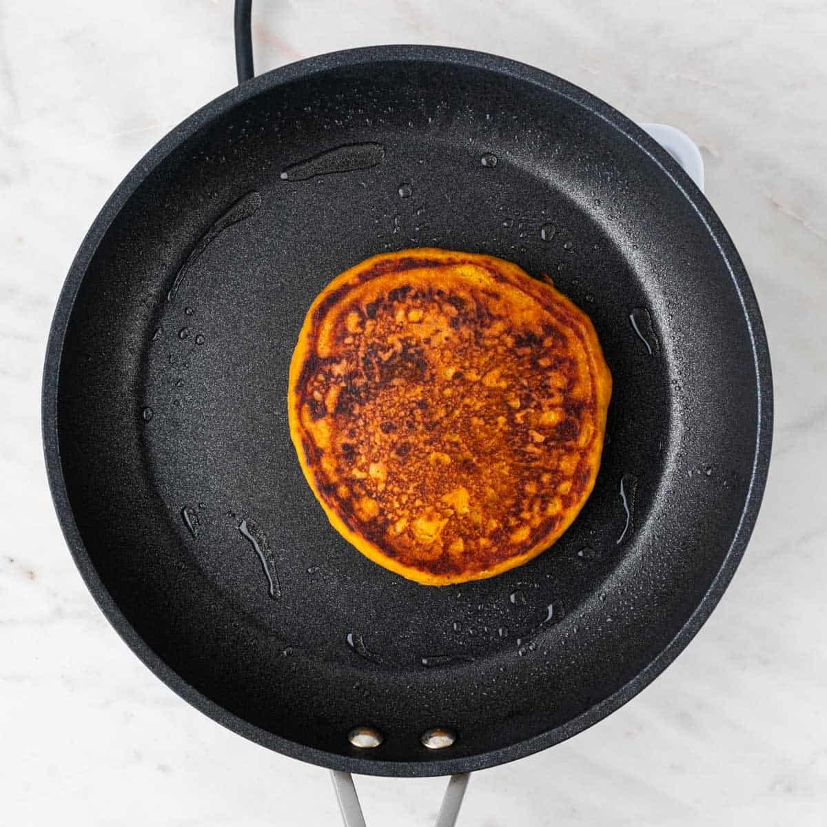 Vegan pumpkin pancake cooking in a greased pan.