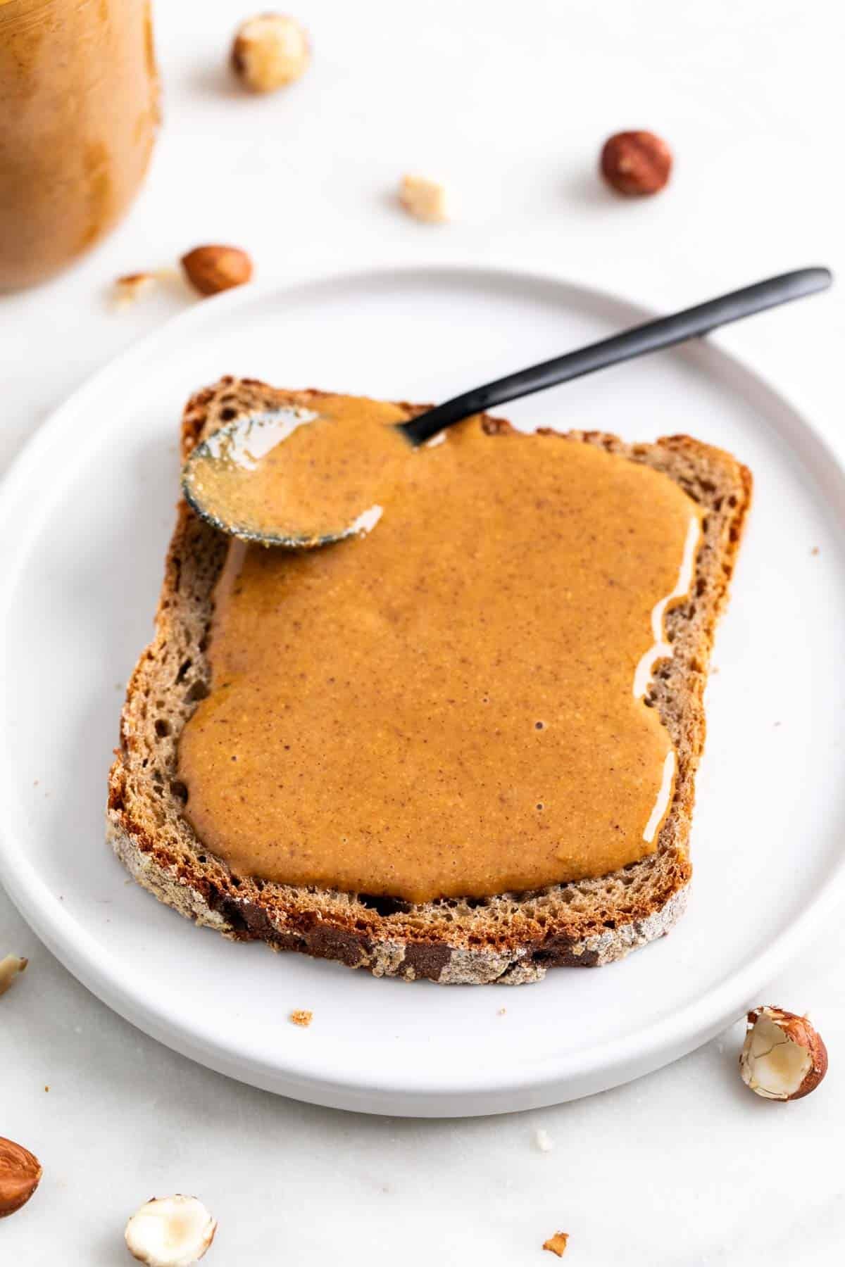 Slice of bread spread with hazelnut butter and a spoon.