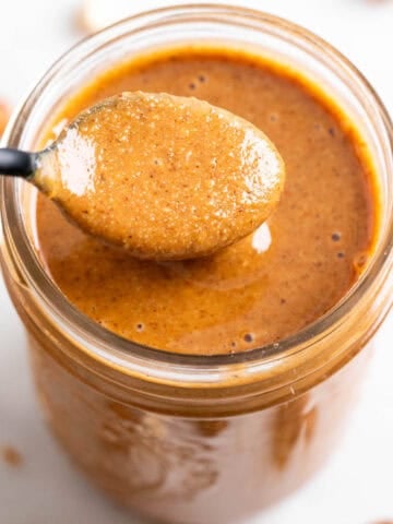 Spoon scooping out hazelnut butter from a jar.