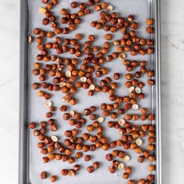 Raw hazelnuts on a lined baking sheet.