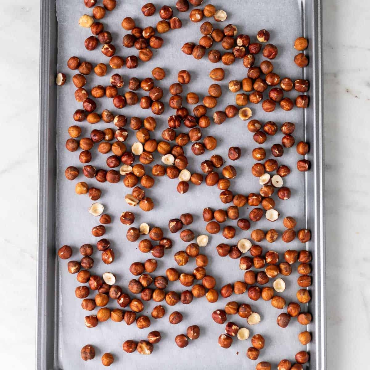 Raw hazelnuts on a lined baking sheet.