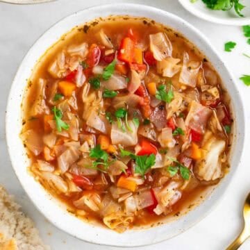 Vegan cabbage soup served with a piece of bread.