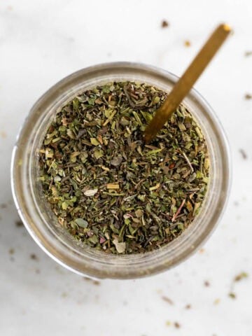 Jar of homemade Italian seasoning with a spoon.