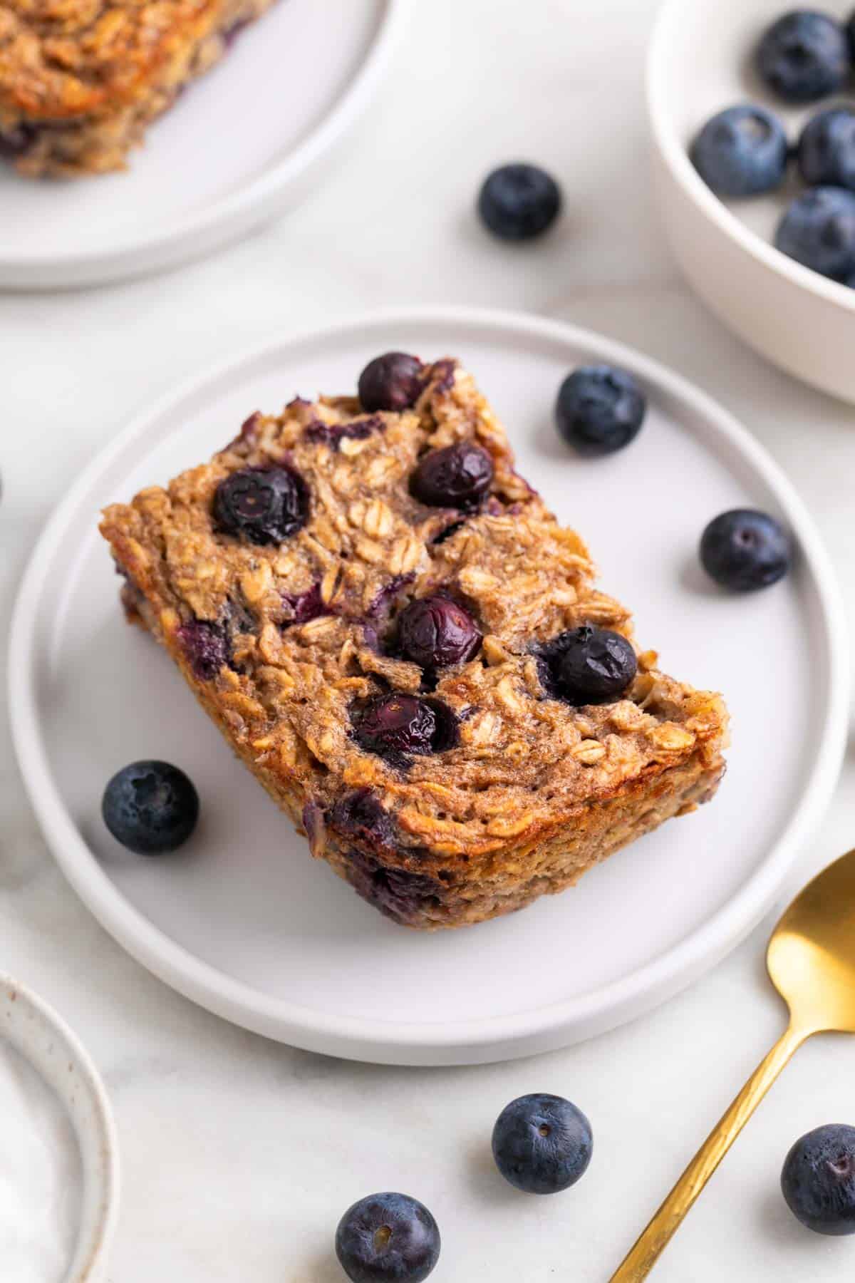 Slice of vegan baked oatmeal served on a plate with blueberries and a spoon.
