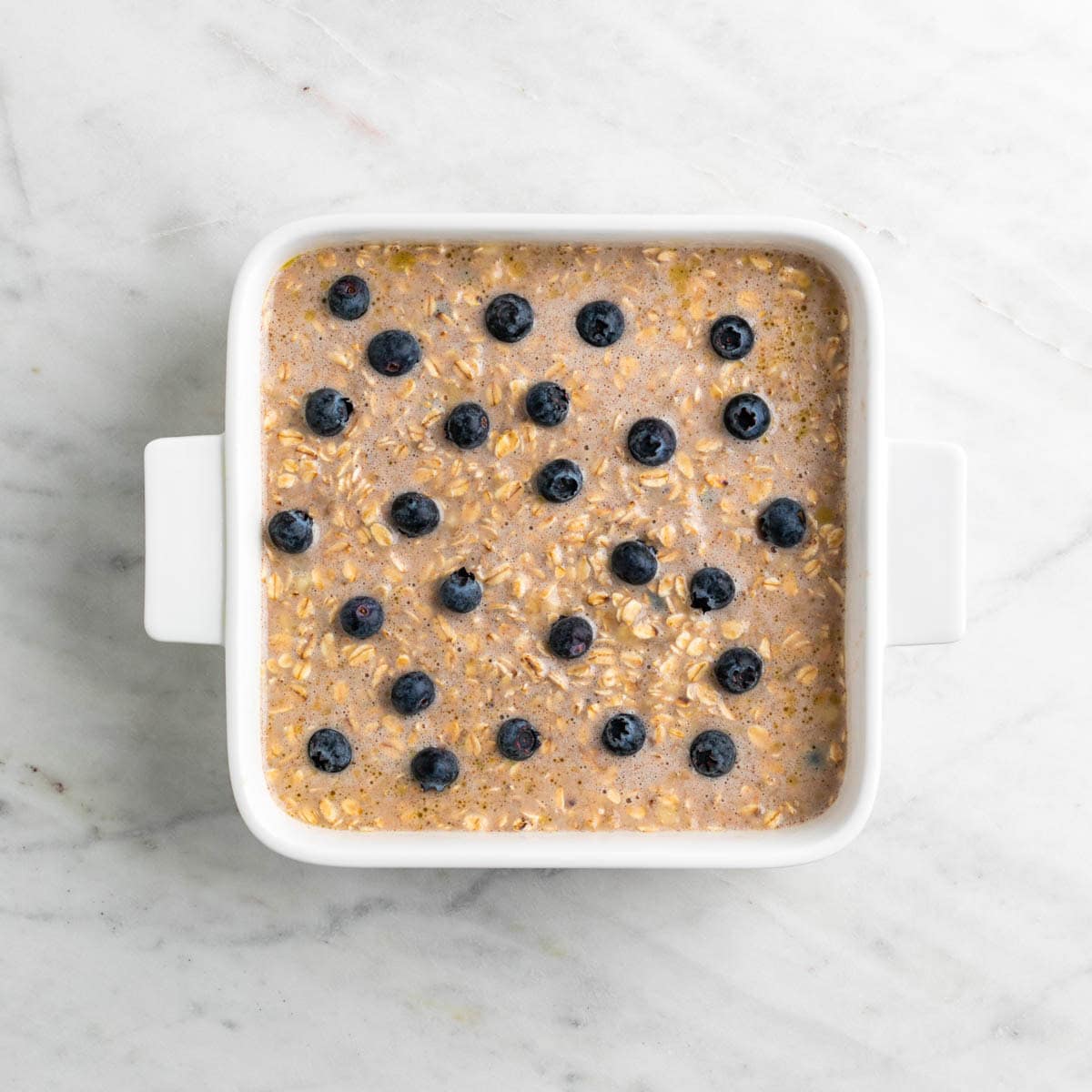 Vegan baked oatmeal mixture in a baking dish topped with blueberries.