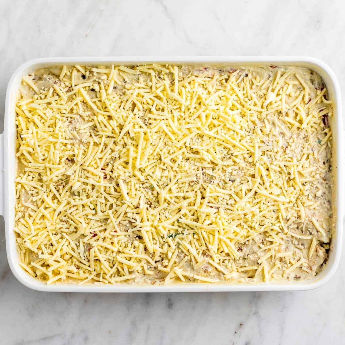 Breakfast casserole topped with vegan cheese before baking.