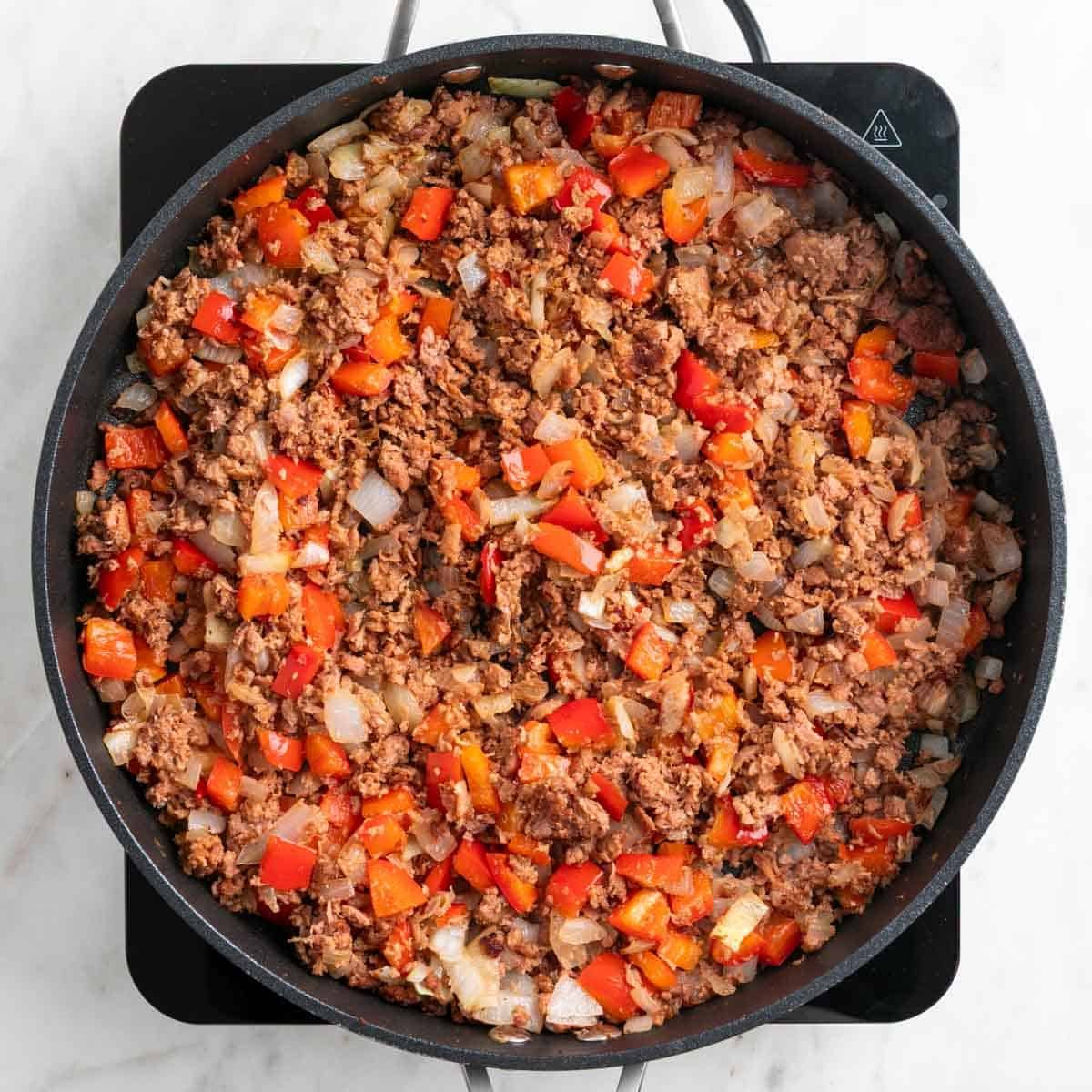 Cooked vegan sausage, onion, and red bell pepper in a skillet.