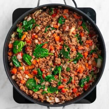 Cooked vegan sausage, onion, red bell pepper, and baby spinach in a skillet.
