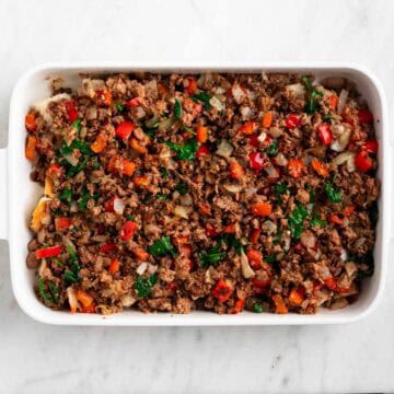 Crusty bread topped with cooked vegan sausage and vegetables in a baking dish.