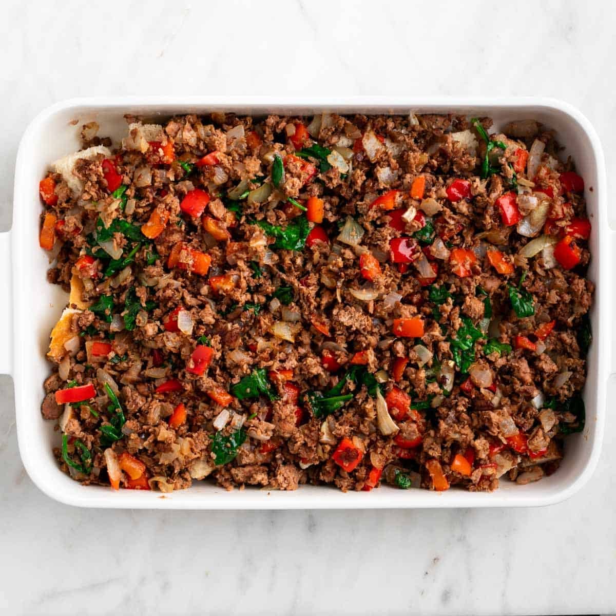 Crusty bread topped with cooked vegan sausage and vegetables in a baking dish.