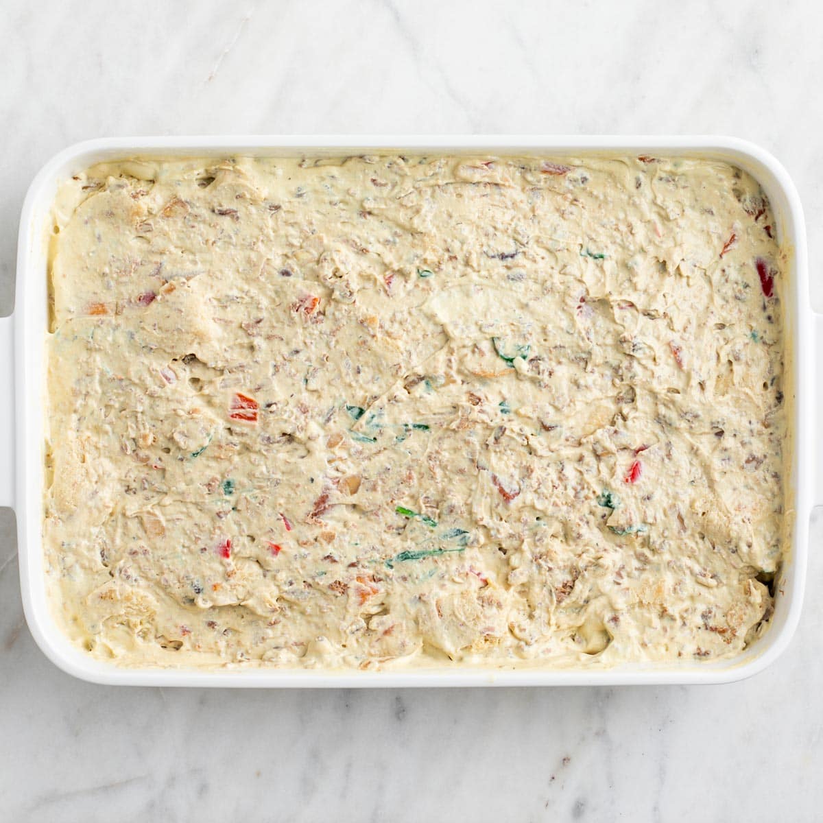 Bread, vegetables, vegan sausage, and tofu mixture combined in a baking dish.