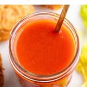 Jar of vegan buffalo sauce with tofu wings and fresh celery.