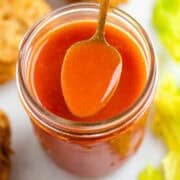 Vegan buffalo sauce being spooned from a jar.