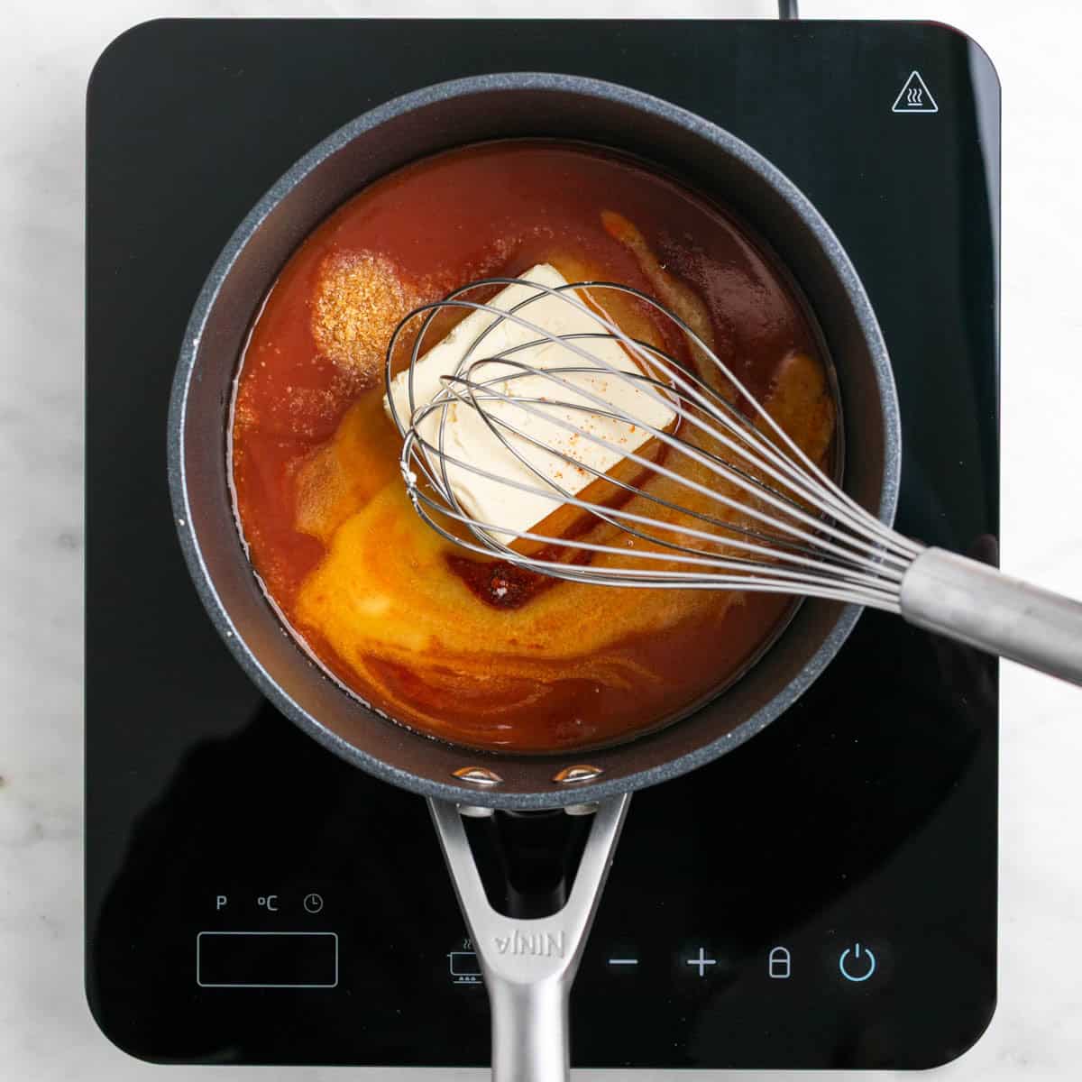 Vegan buffalo sauce ingredients being whisked in a saucepan.