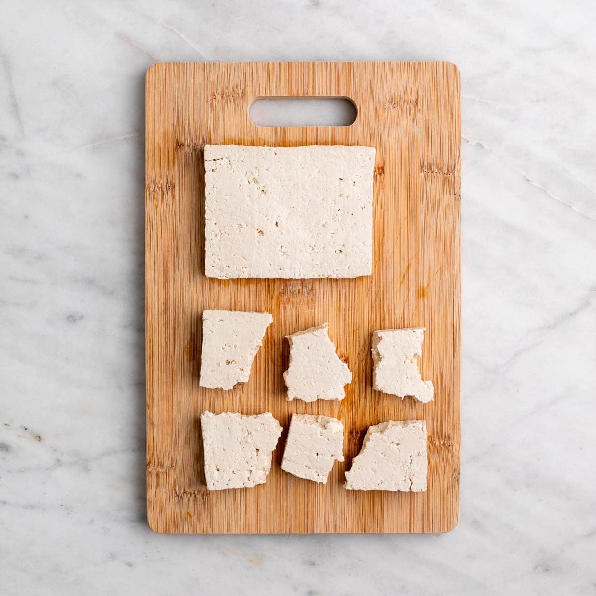 Wooden cutting board with a slab of tofu and tofu pieces cut into wings.