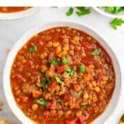Vegan lentil soup plated in a bowl with crusty bread and fresh parsley.
