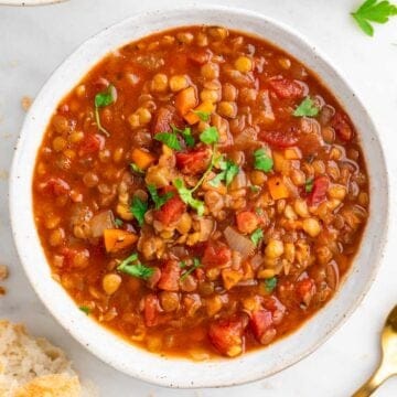 Bowl of vegan lentil soup garnished with parsley, with bread on the side.