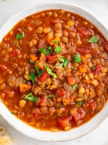 Bowl of vegan lentil soup garnished with parsley, with bread on the side.