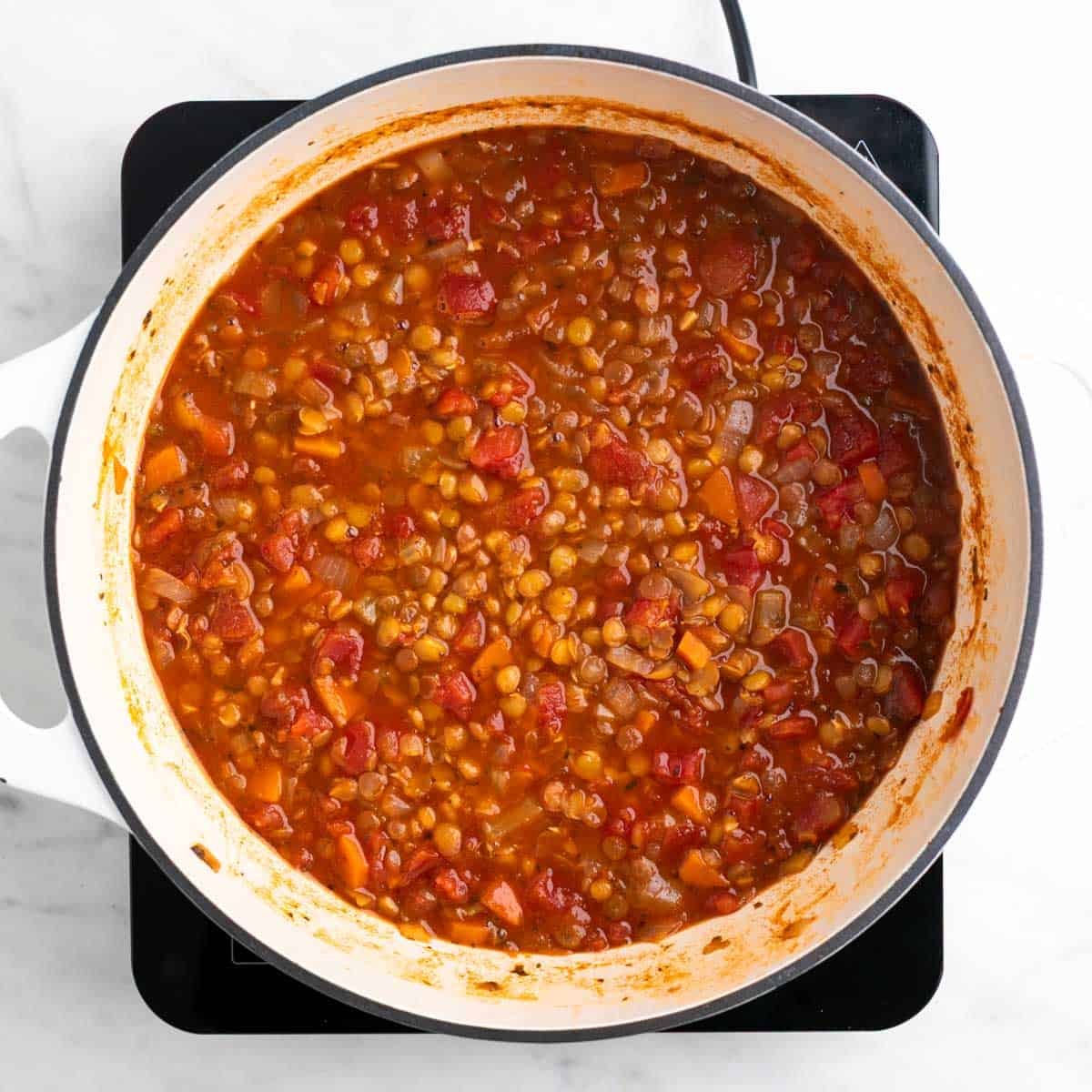 Cooked vegan lentil soup in a large pot before adding salt and black pepper.