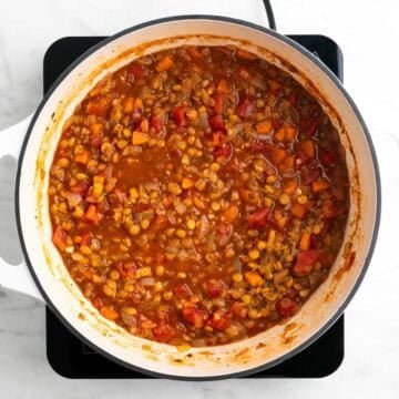 Cooked vegan lentil soup seasoned with salt and black pepper in a large pot.
