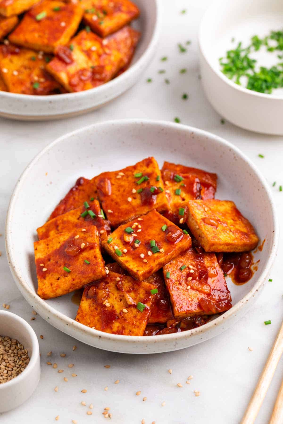 Spicy tofu garnished with sesame seeds and chives, served with chopsticks.