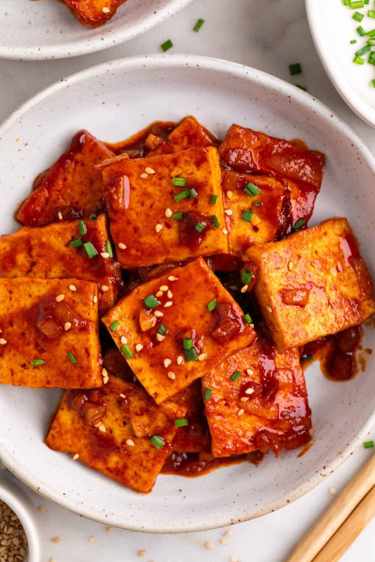 Spicy tofu topped with sesame seeds and chives, chopsticks on the side.
